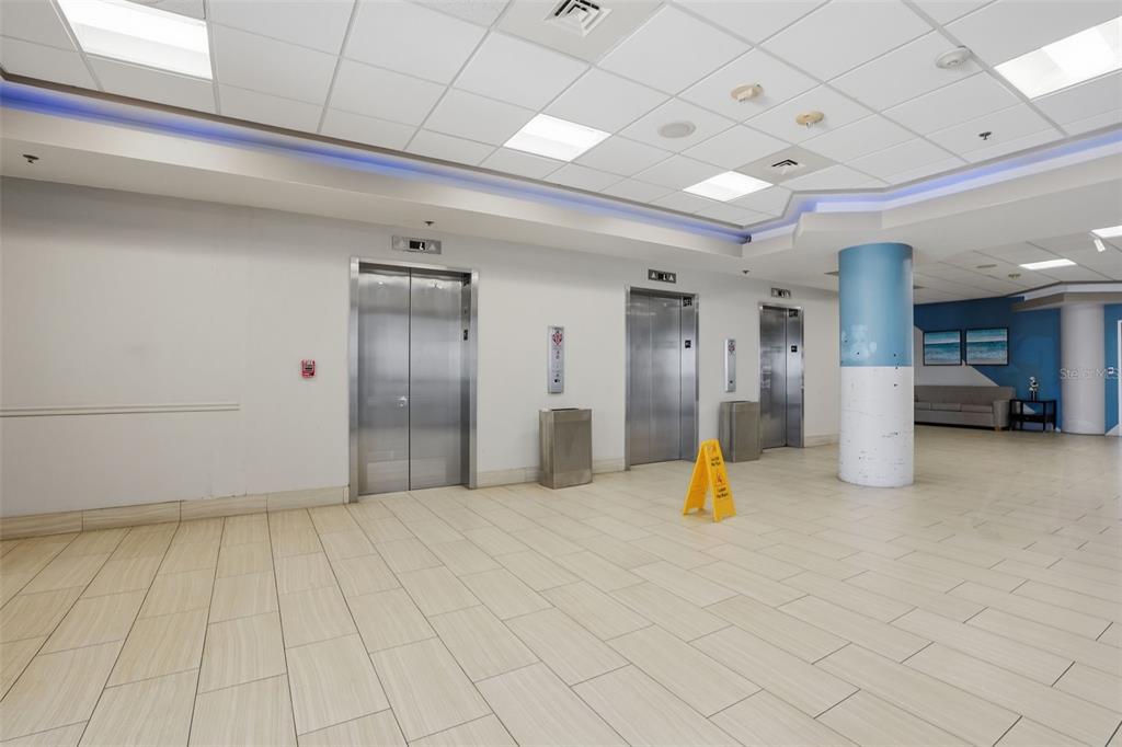A commercial lobby features three stainless steel elevators, light tile flooring, and a blue column — 2700 N ATLANTIC AVENUE UNIT 407, DAYTONA BEACH, FL