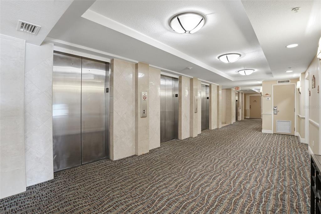 A hallway with carpeted flooring, three stainless steel elevator doors, and beige tiled walls — 2700 N ATLANTIC AVENUE UNIT 407, DAYTONA BEACH, FL