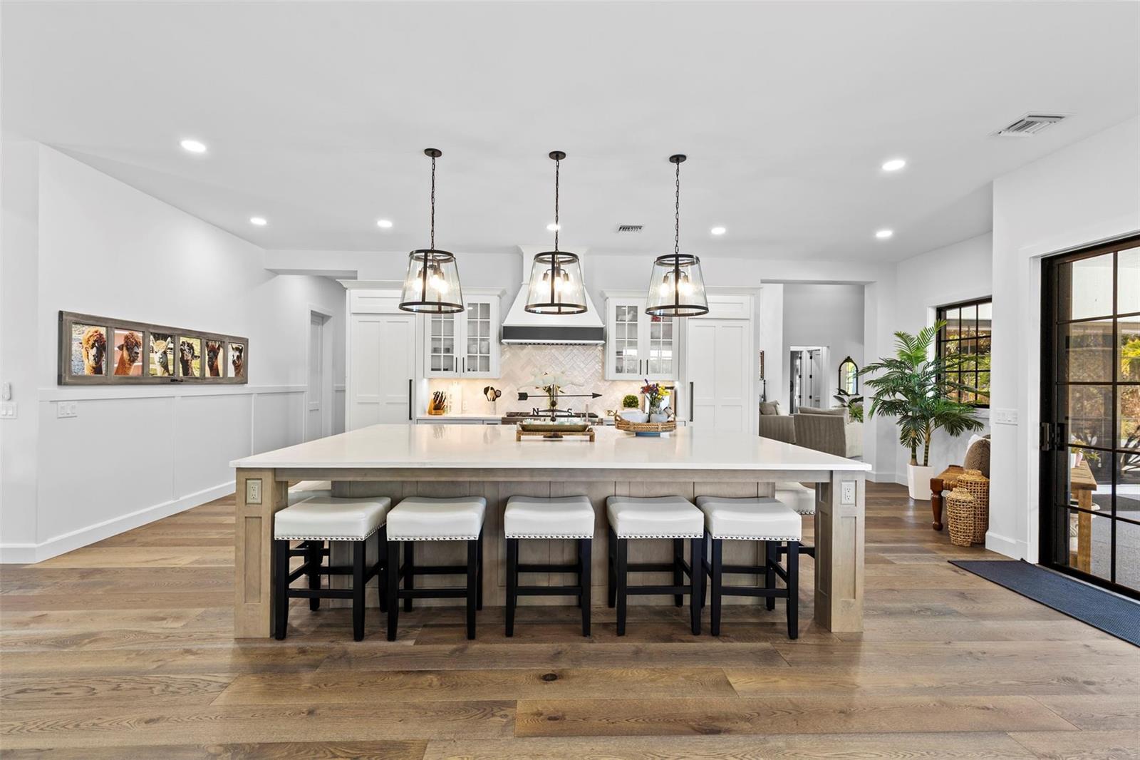 A modern kitchen features a large central island with five stools and white cabinetry — 14473 Draft Horse Lane, Wellington FL 33414, WELLINGTON, FL