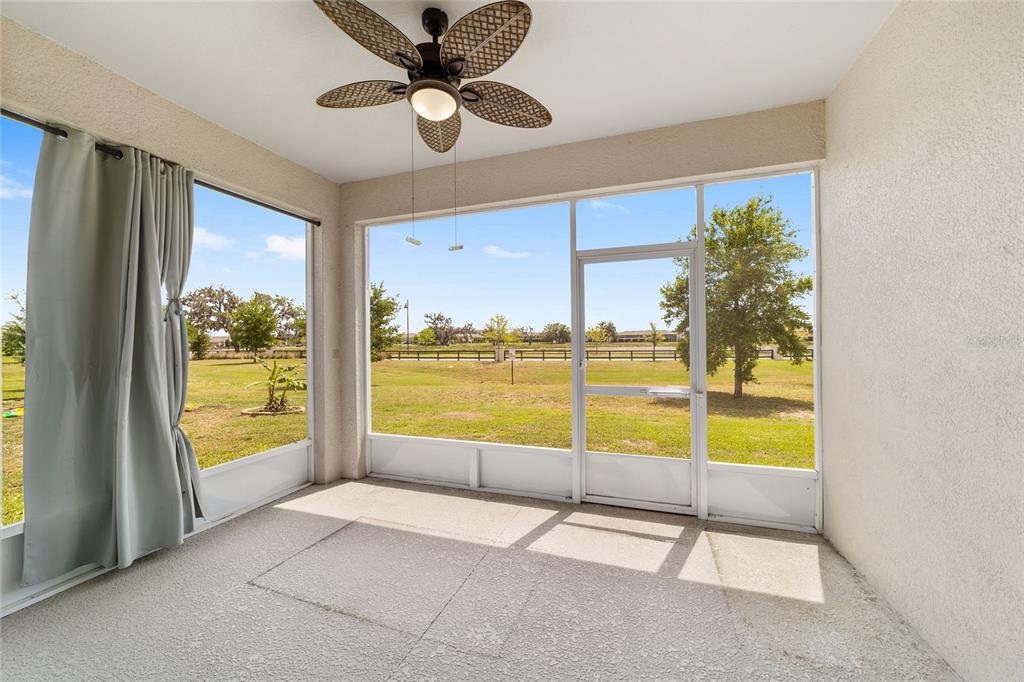 A screened-in porch features a ceiling fan, light-colored walls, and views of a grassy yard — 5051 STOKES WAY, WILDWOOD, FL