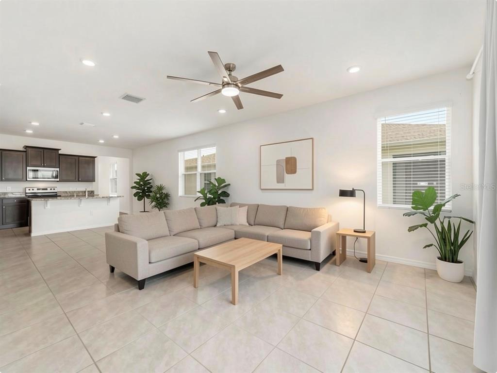An open-concept living room features a sectional sofa, coffee table, and tile flooring — 5051 STOKES WAY, WILDWOOD, FL
