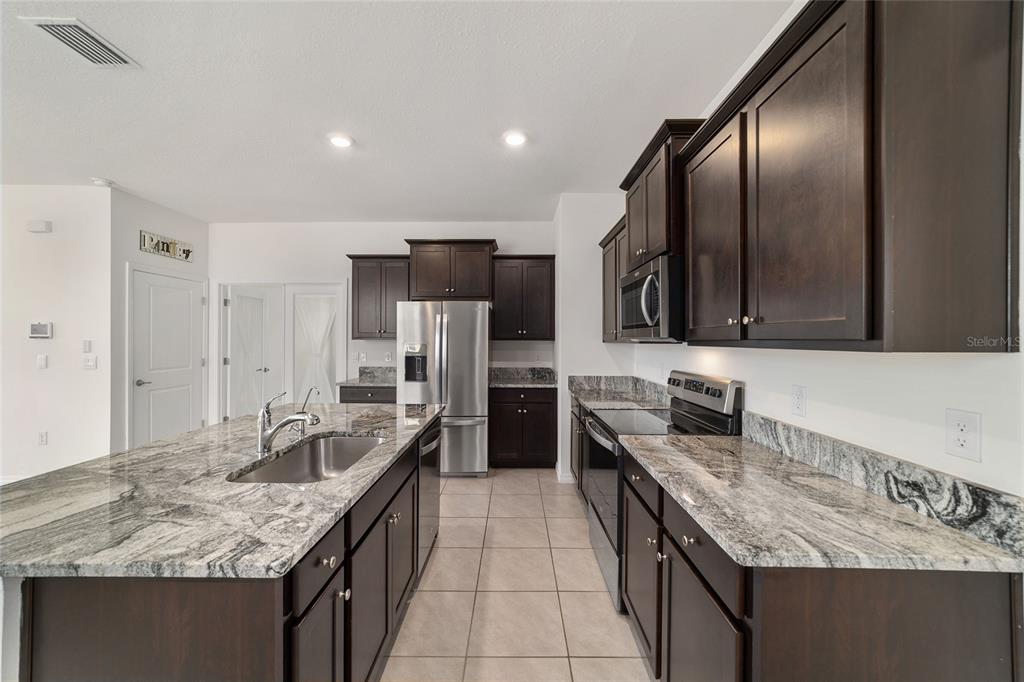 A kitchen featuring dark wood cabinets, granite countertops, stainless steel appliances, and a central island — 5051 STOKES WAY, WILDWOOD, FL