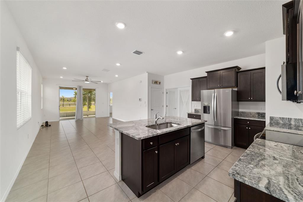 A kitchen with dark cabinets and granite countertops overlooks an open-concept living area with tile — 5051 STOKES WAY, WILDWOOD, FL