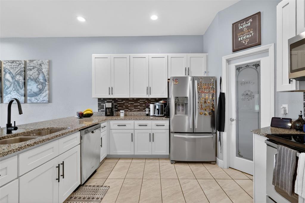 A kitchen with white cabinets, granite countertops, stainless steel appliances, and a pantry door — 1028 GREEN GATE BOULEVARD, GROVELAND, FL