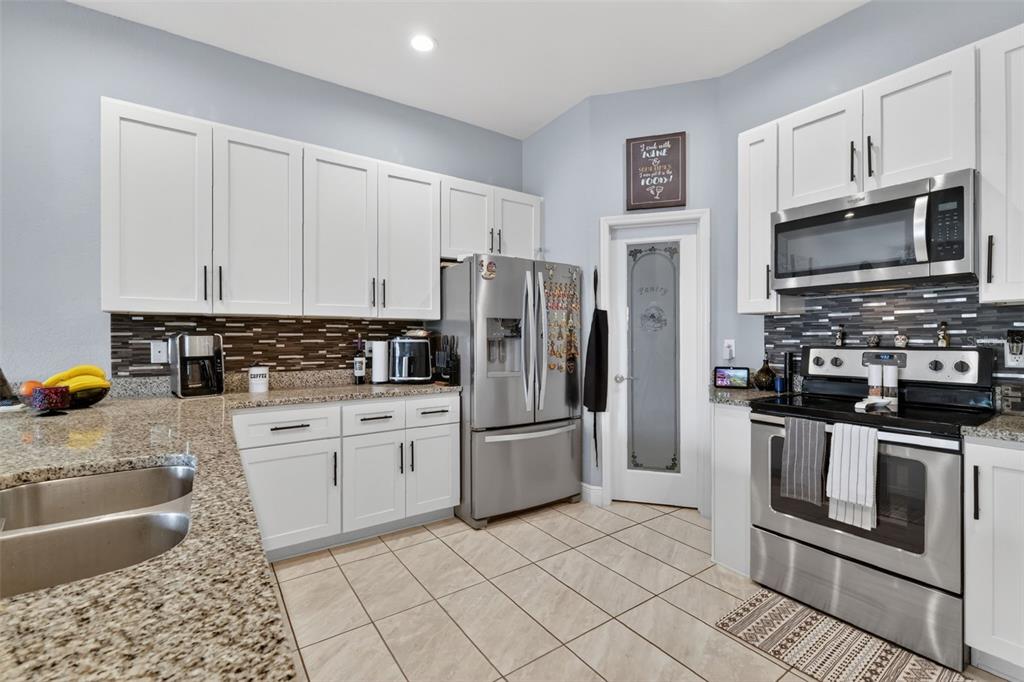 A kitchen features white cabinets, stainless steel appliances, granite countertops, and a tiled floor — 1028 GREEN GATE BOULEVARD, GROVELAND, FL