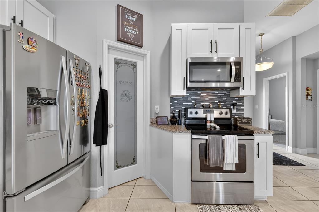 A kitchen features stainless steel appliances, white cabinetry, a pantry door, and granite countertops — 1028 GREEN GATE BOULEVARD, GROVELAND, FL