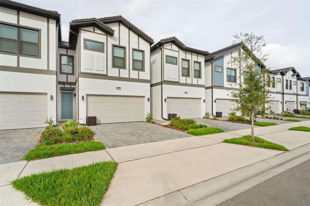 A row of modern two-story townhomes with white stucco facades, dark trim, and paved driveways — 10467 EBB TIDE LANE, ORLANDO, FL