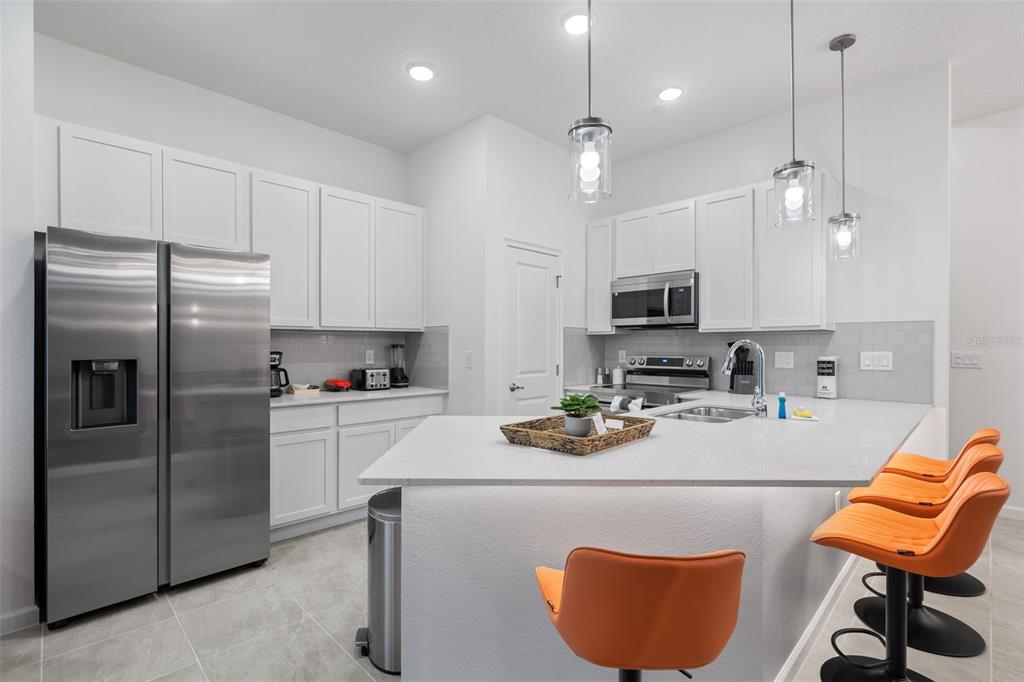 A modern kitchen features white cabinetry, stainless steel appliances, a quartz island, and orange stools — 10467 EBB TIDE LANE, ORLANDO, FL