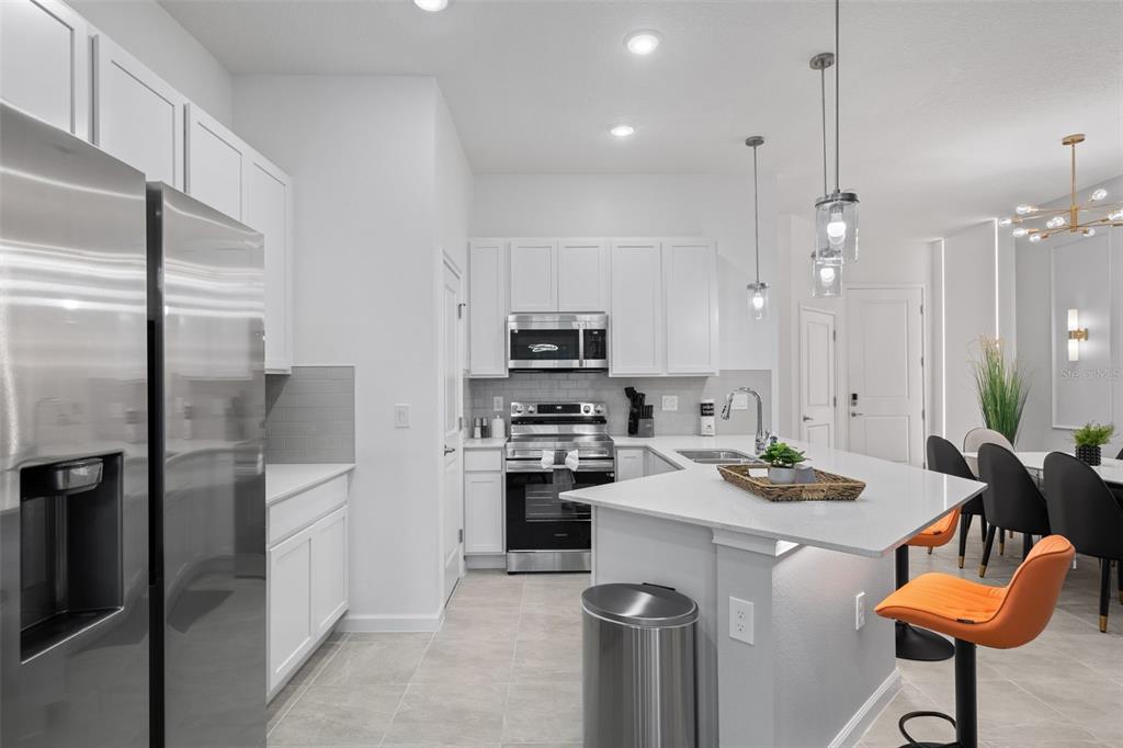 A modern kitchen features white cabinets, stainless steel appliances, a quartz island, and orange stools — 10467 EBB TIDE LANE, ORLANDO, FL