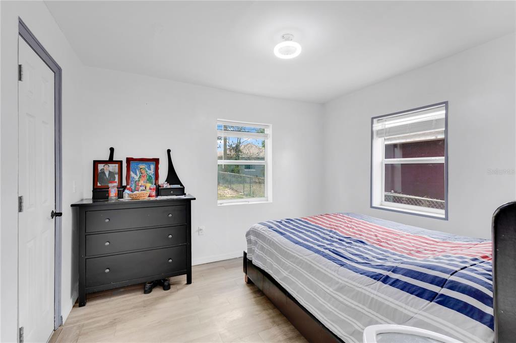 A bedroom features light wood-look flooring, white walls, a black dresser, and a striped bedspread — 423 N 5TH STREET, HAINES CITY, FL