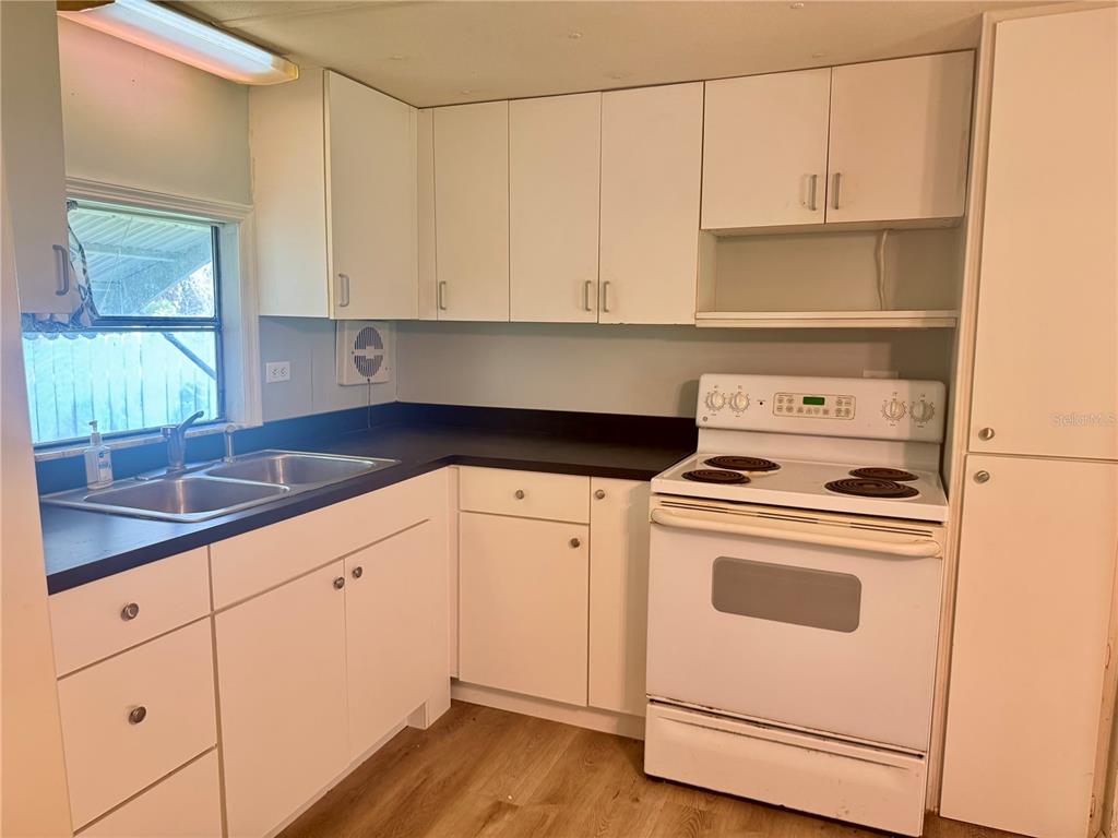 A kitchen features white cabinets, a black countertop, a double sink, and a white stove — 3405 FREMONT LANE, SPRING HILL, FL