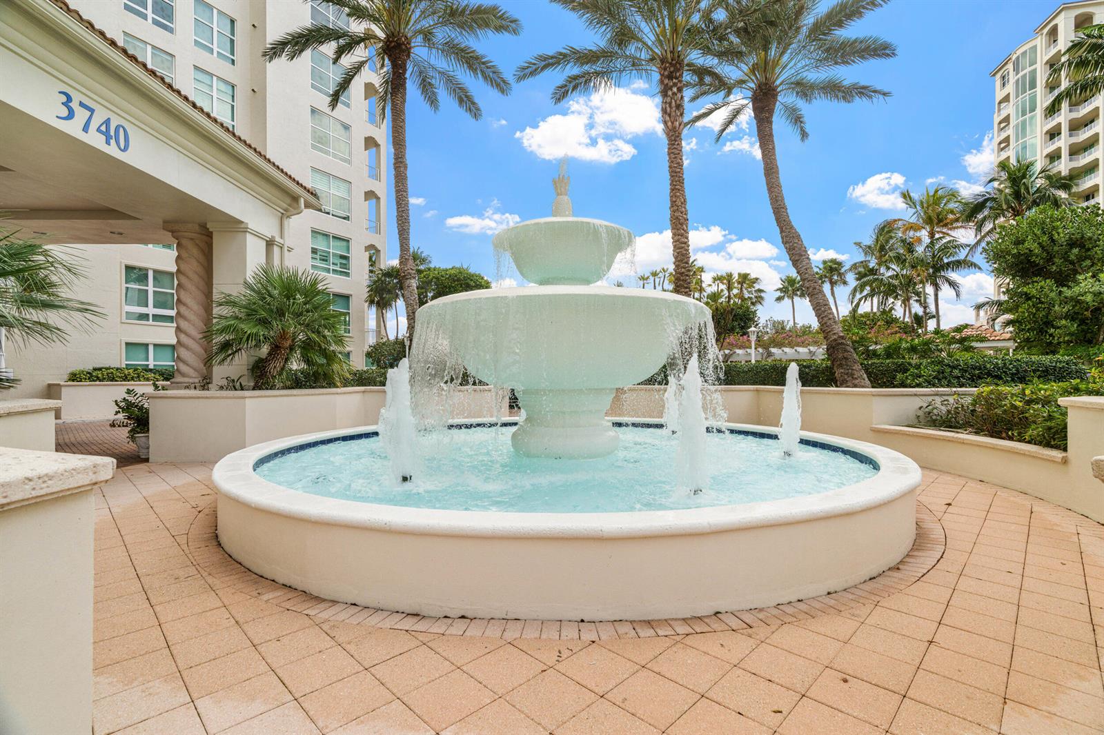 A tiered white fountain sits in a paved courtyard in front of a multi-story building — 3740 S Ocean Boulevard Apt 709, Highland Beach FL 33487, HIGHLAND BEACH, FL
