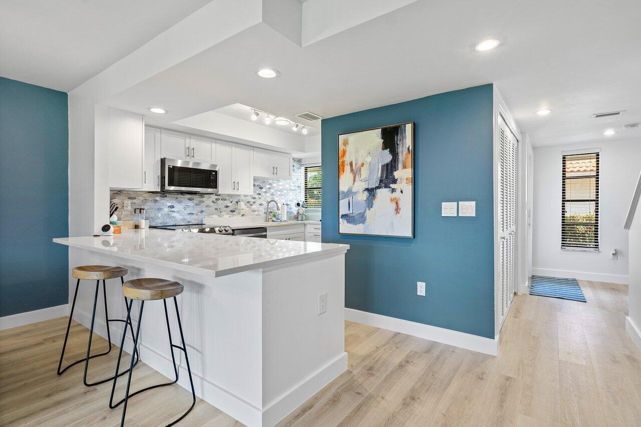 A kitchen with white cabinets, a quartz island, and blue accent walls with abstract art — 4143 Kittiwake Court, Boynton Beach FL 33436, BOYNTON BEACH, FL