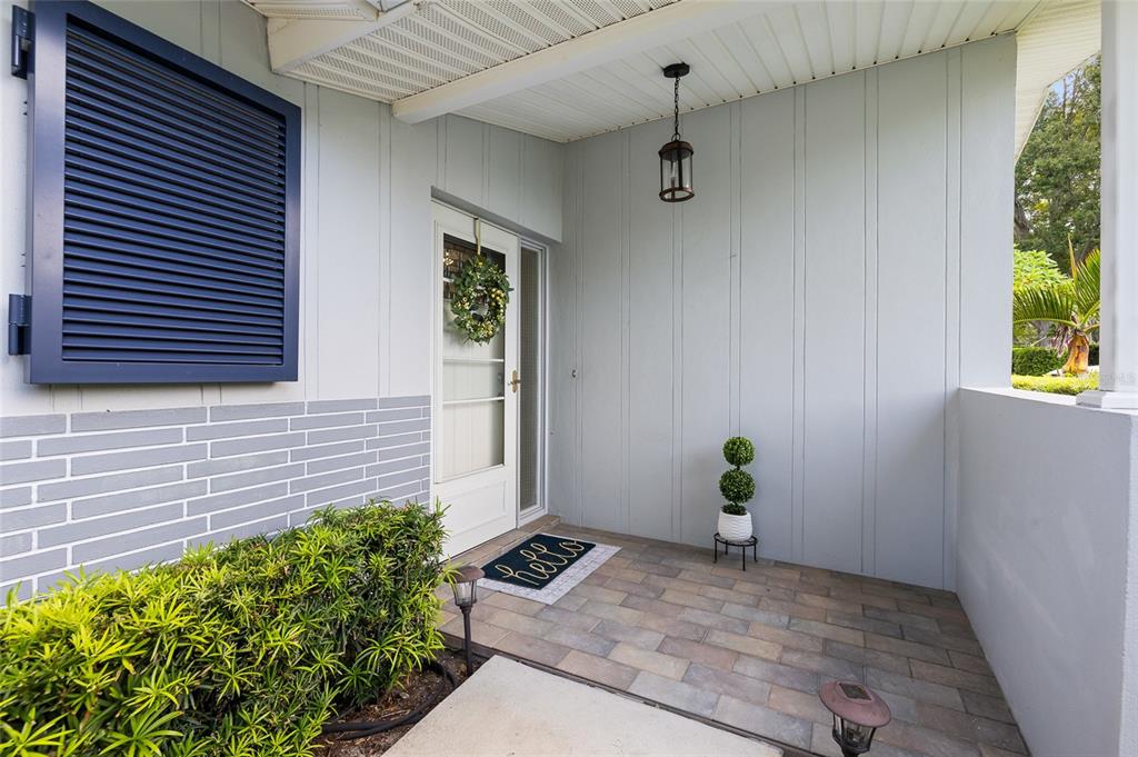 A covered front porch features light-colored vertical siding, a brick-patterned wall, and a paved floor — 1394 BELLEVUE BOULEVARD, CLEARWATER, FL