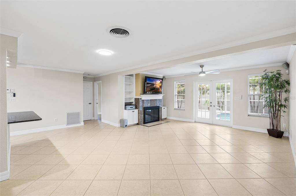 A spacious living room with tile floors, a fireplace, built-in shelving, and glass patio doors — 1394 BELLEVUE BOULEVARD, CLEARWATER, FL