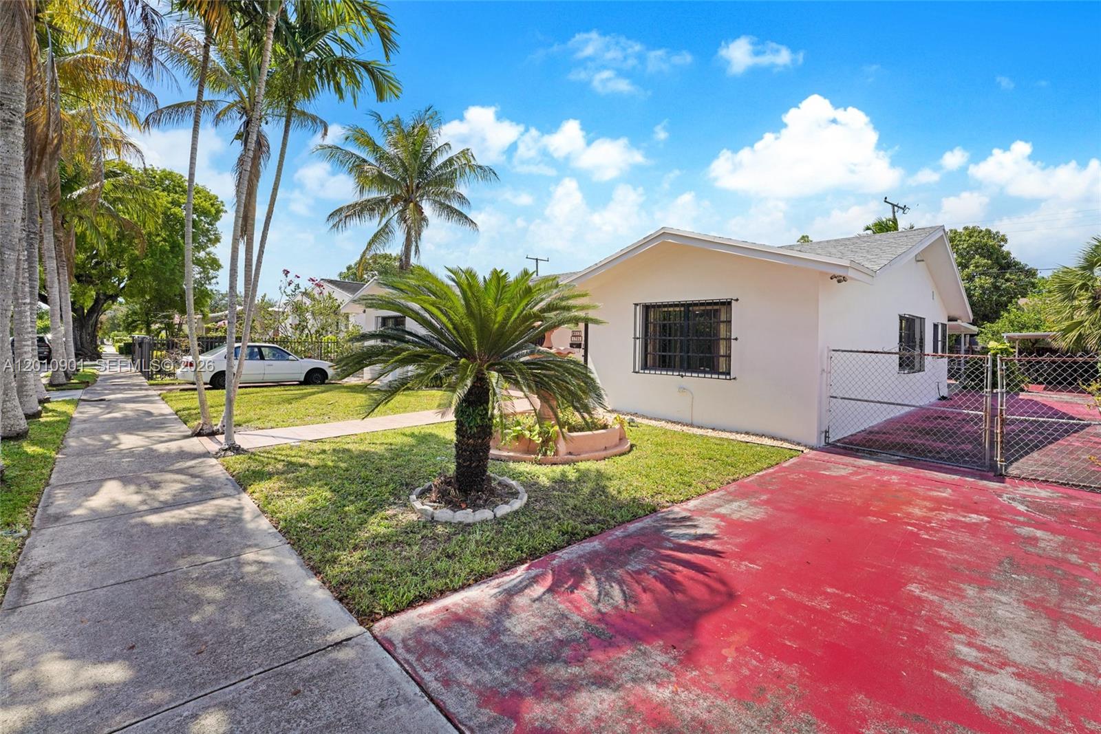A single-story white house features a red driveway, a chain-link fence, and palm trees — 1735 SW 15th St, Miami FL 33145, MIAMI, FL