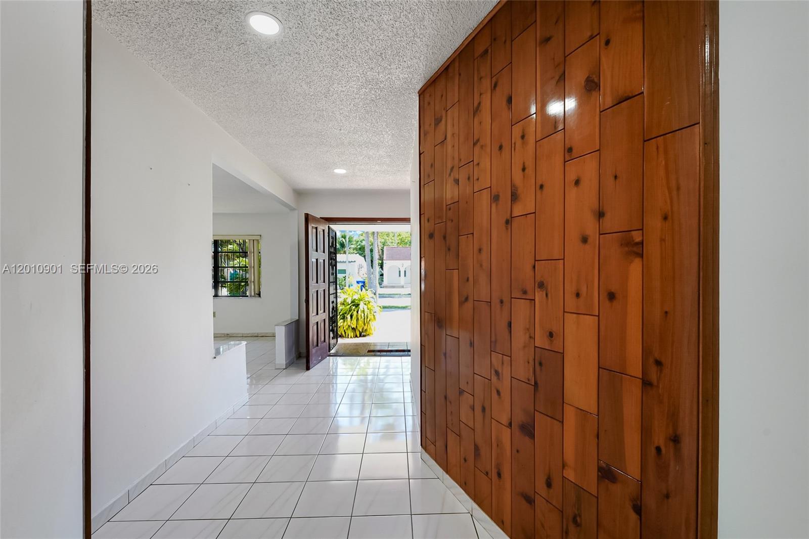 A bright entryway features white tile floors, a textured ceiling, and a wood-paneled accent wall — 1735 SW 15th St, Miami FL 33145, MIAMI, FL