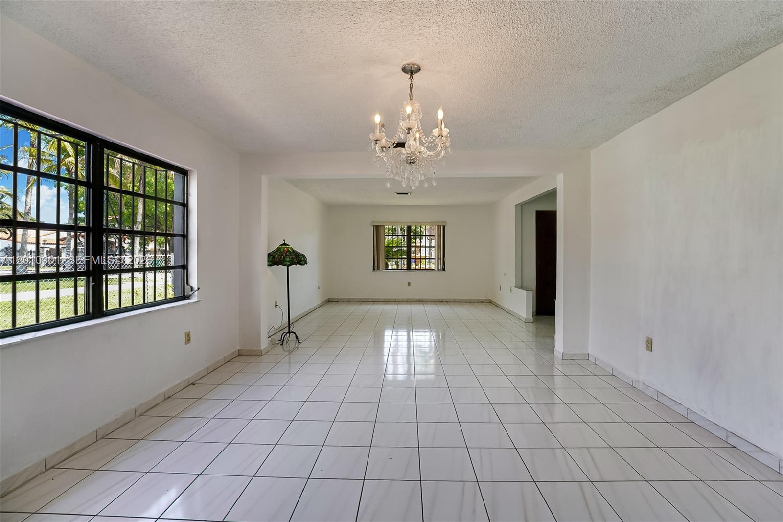 An empty room features white tile floors, white walls, a crystal chandelier, and barred windows — 1735 SW 15th St, Miami FL 33145, MIAMI, FL