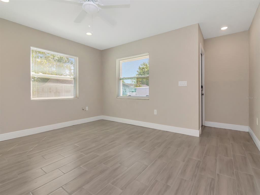An empty room features light-colored walls, wood-look tile flooring, two windows, and a ceiling fan — 1211 62ND AVENUE E, BRADENTON, FL