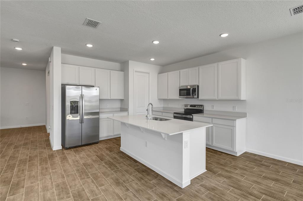 A modern kitchen features white cabinetry, stainless steel appliances, a center island, and wood-look flooring — 6170 DAPHNE STREET, LAKE HAMILTON, FL