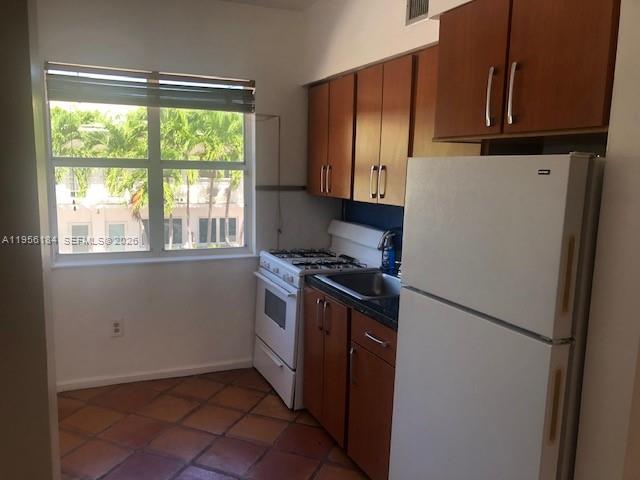 A kitchen features wood cabinets, a white refrigerator, a gas stove, and tile flooring — 736 13th St # 202, Miami Beach FL 33139, MIAMI BEACH, FL