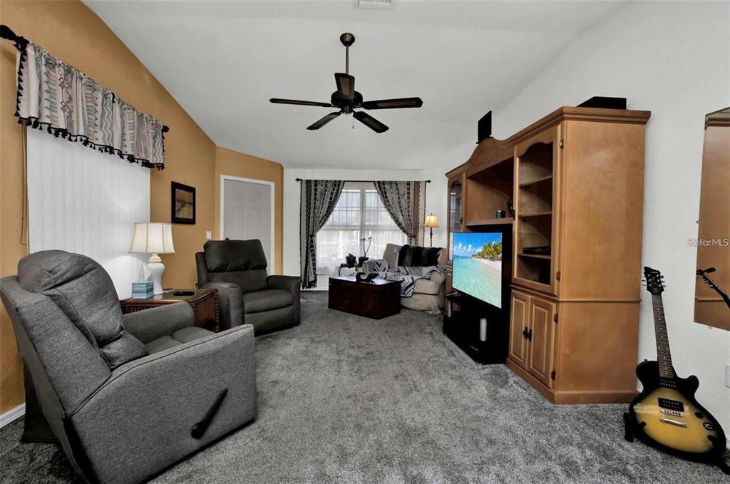 A living room features gray carpet, two recliners, a wooden entertainment center, and a guitar — 3520 KENNETH ROAD, PORT CHARLOTTE, FL