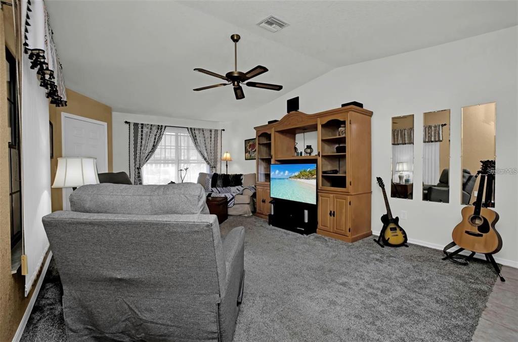 A living room features gray carpeting, a large wooden entertainment center, and two guitars — 3520 KENNETH ROAD, PORT CHARLOTTE, FL