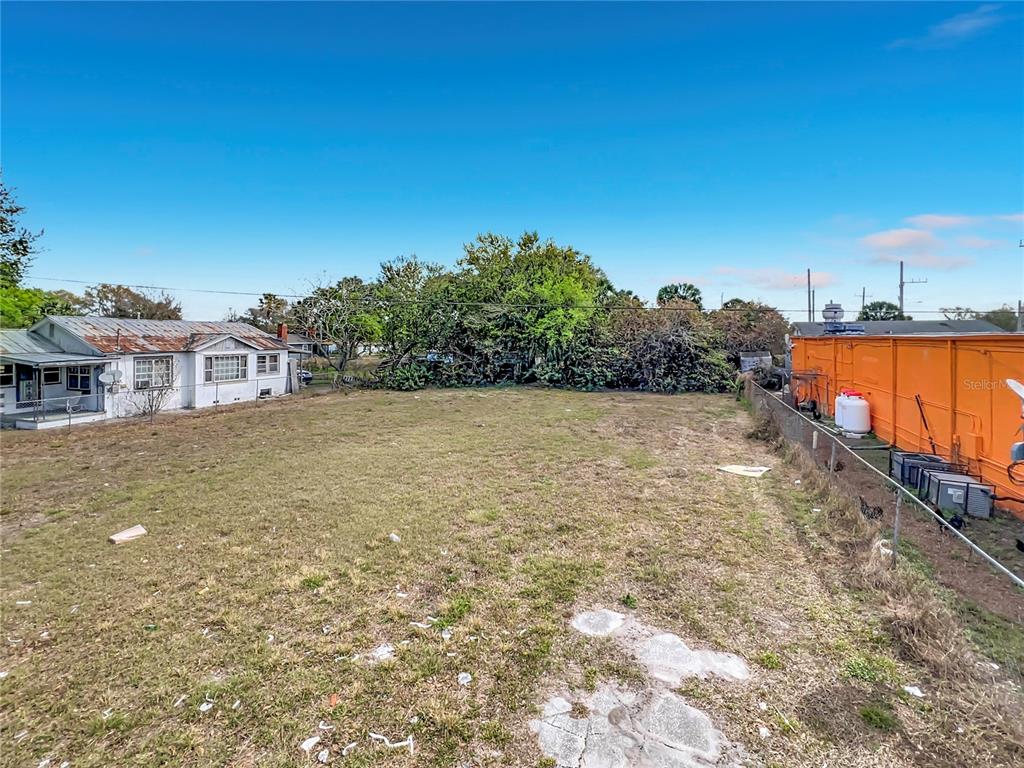 A vacant, grassy lot sits between a small white house and an orange storage container — 2471 GREENWAY STREET, SANFORD, FL