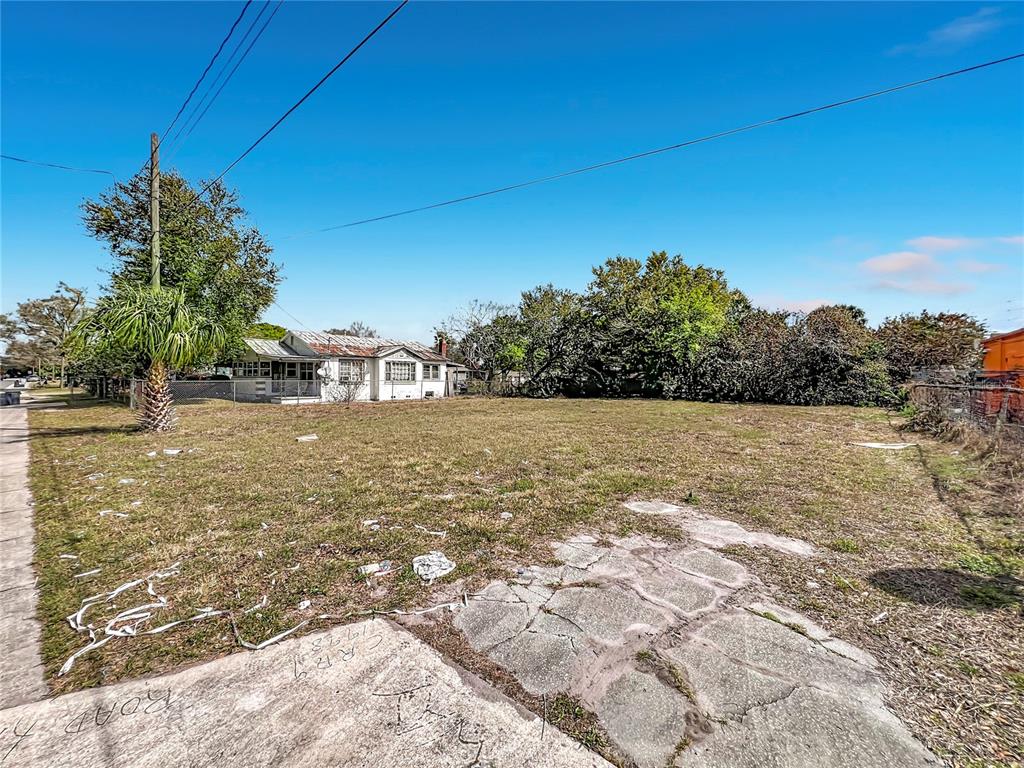A vacant, grassy lot sits in front of a small, older house under a blue sky — 2471 GREENWAY STREET, SANFORD, FL