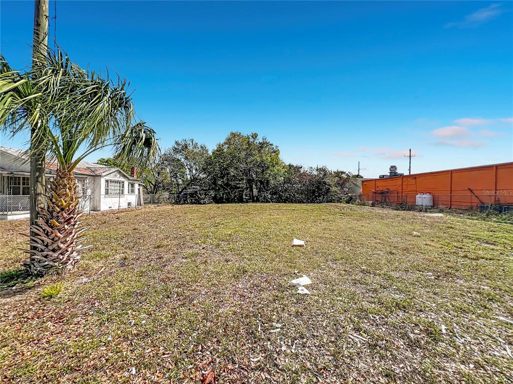 A vacant, grassy lot sits next to a small house and a large orange wall — 2471 GREENWAY STREET, SANFORD, FL