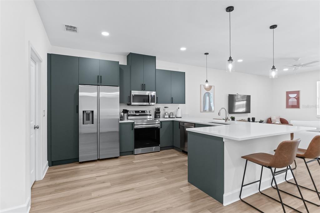 A modern kitchen features dark teal cabinets, stainless steel appliances, and a white quartz island — 11421 & 11423 WELDON STREET, SEFFNER, FL