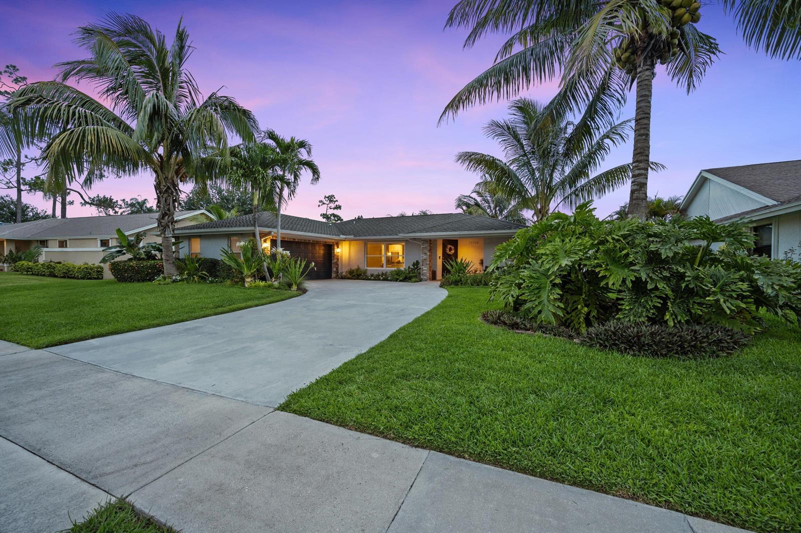 A single-story house with a concrete driveway, palm trees, and a manicured lawn at dusk — 14244 Horseshoe Trace, Wellington FL 33414, WELLINGTON, FL