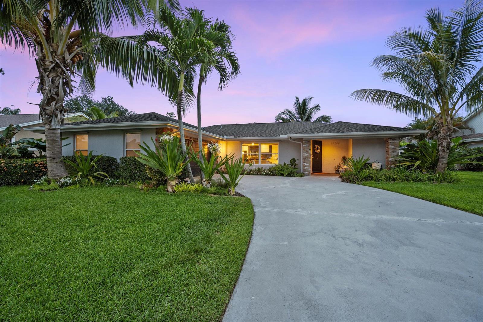 A single-story house with a concrete driveway, palm trees, and a lawn at dusk — 14244 Horseshoe Trace, Wellington FL 33414, WELLINGTON, FL