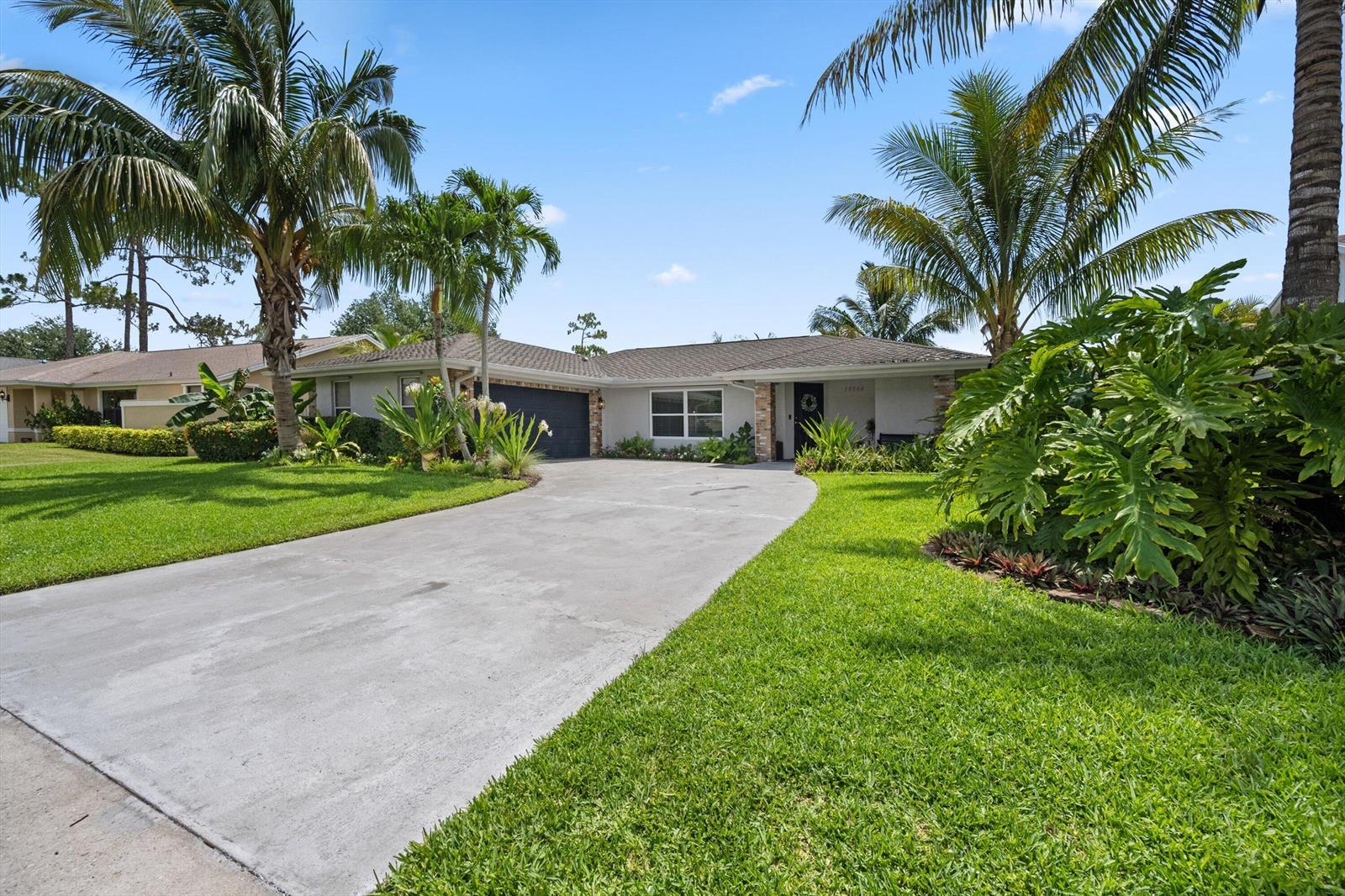 A single-story house with a concrete driveway, palm trees, and lush landscaping under a blue sky — 14244 Horseshoe Trace, Wellington FL 33414, WELLINGTON, FL