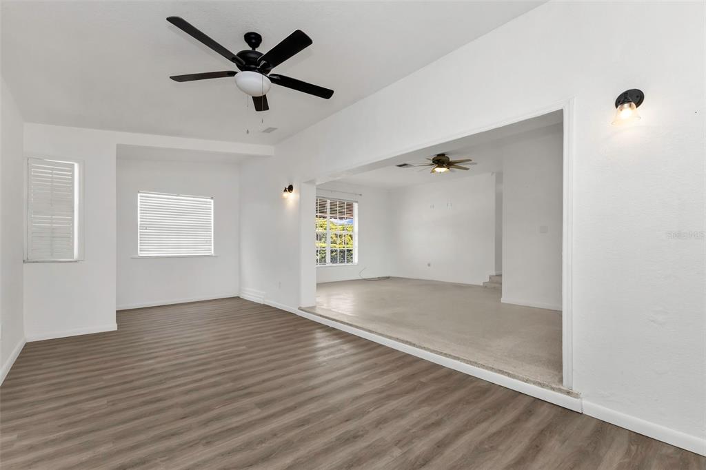 A living room with wood-look flooring transitions into a carpeted sunken room with a ceiling fan — 21533 MIDWAY BOULEVARD, PORT CHARLOTTE, FL