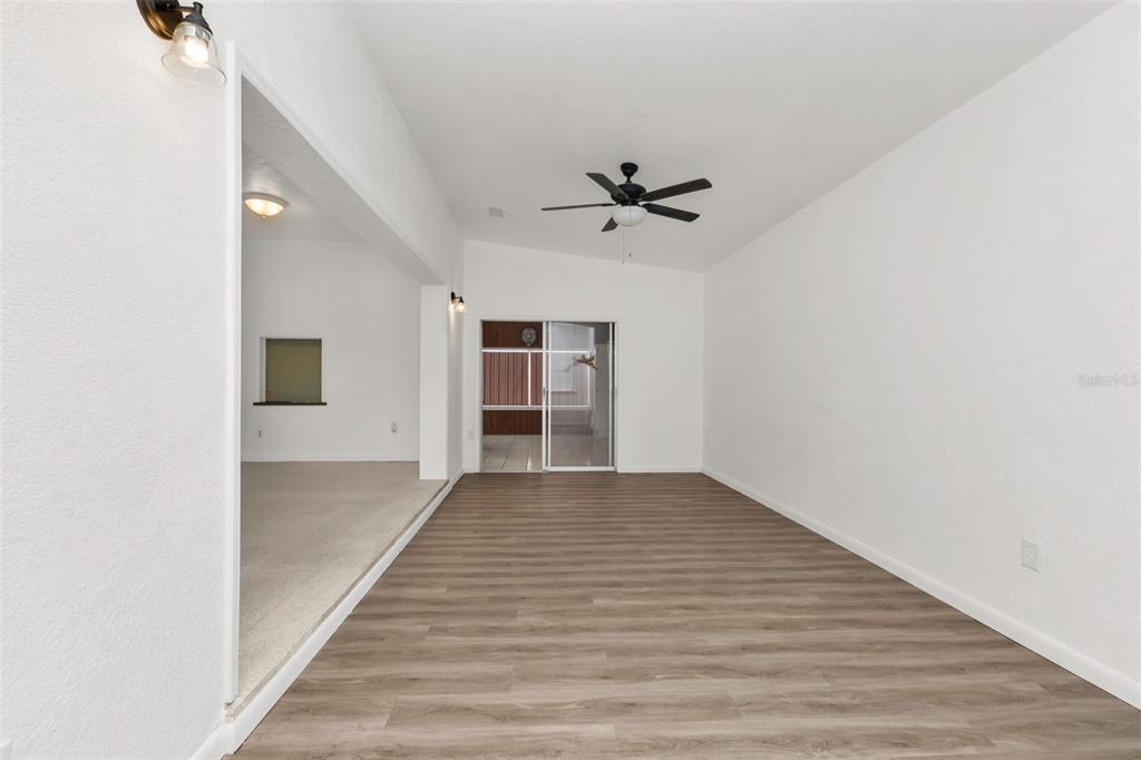 A living room with wood-look flooring, a ceiling fan, and an adjacent carpeted room — 21533 MIDWAY BOULEVARD, PORT CHARLOTTE, FL