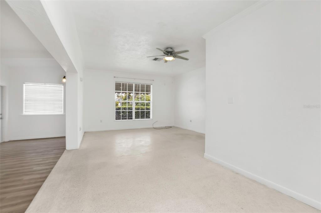 A bright, empty living room features beige carpeting, white walls, and a ceiling fan — 21533 MIDWAY BOULEVARD, PORT CHARLOTTE, FL