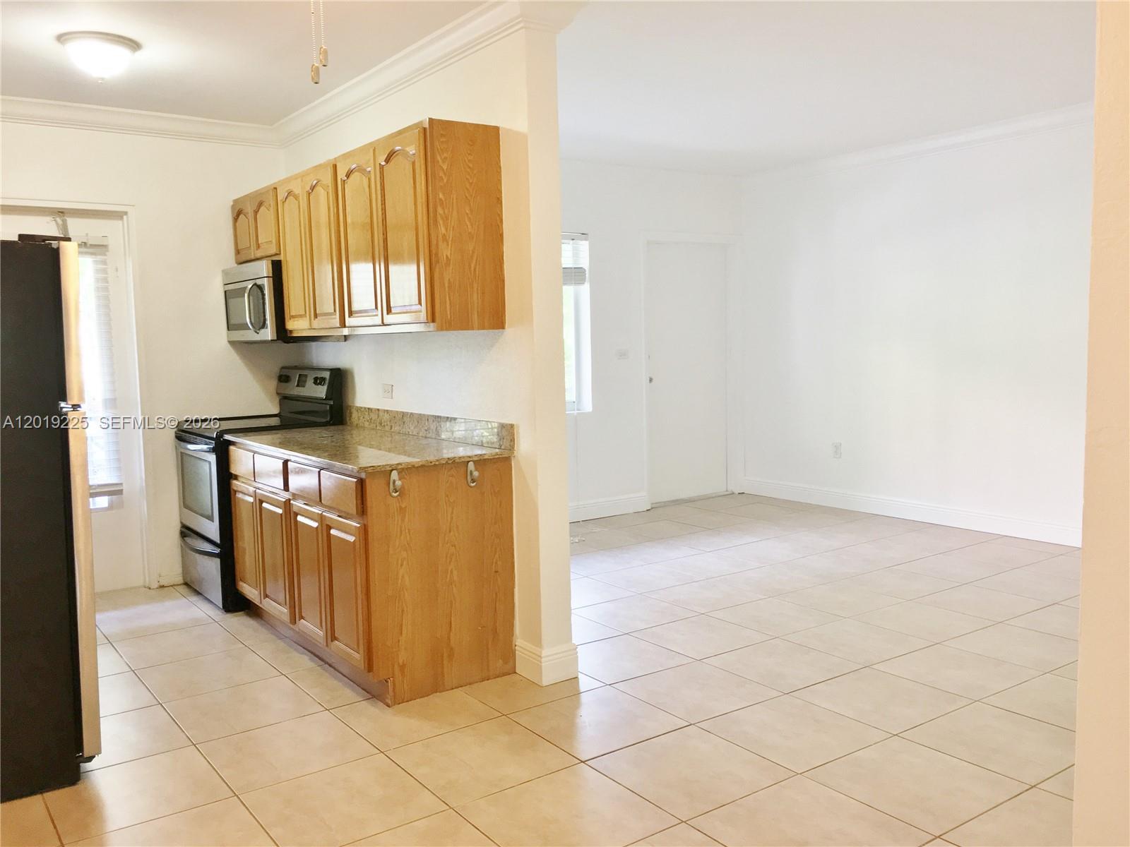 A kitchen with wood cabinets and granite countertops opens into an adjacent tiled living area — 95 Edgewater Dr # 207, Coral Gables FL 33133, CORAL GABLES, FL