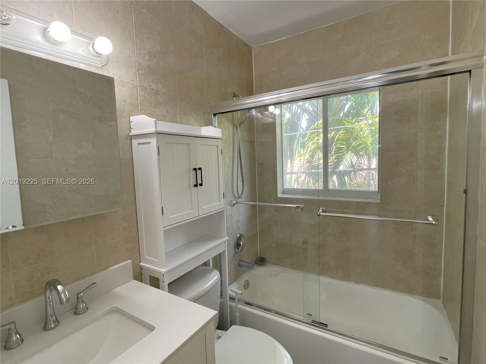 A bathroom features a vanity, a toilet with a storage unit, and a tiled tub-shower — 95 Edgewater Dr # 207, Coral Gables FL 33133, CORAL GABLES, FL
