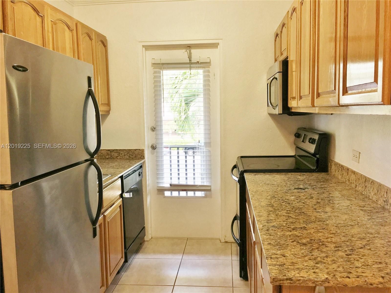 A galley kitchen features light wood cabinets, granite countertops, and stainless steel appliances — 95 Edgewater Dr # 207, Coral Gables FL 33133, CORAL GABLES, FL
