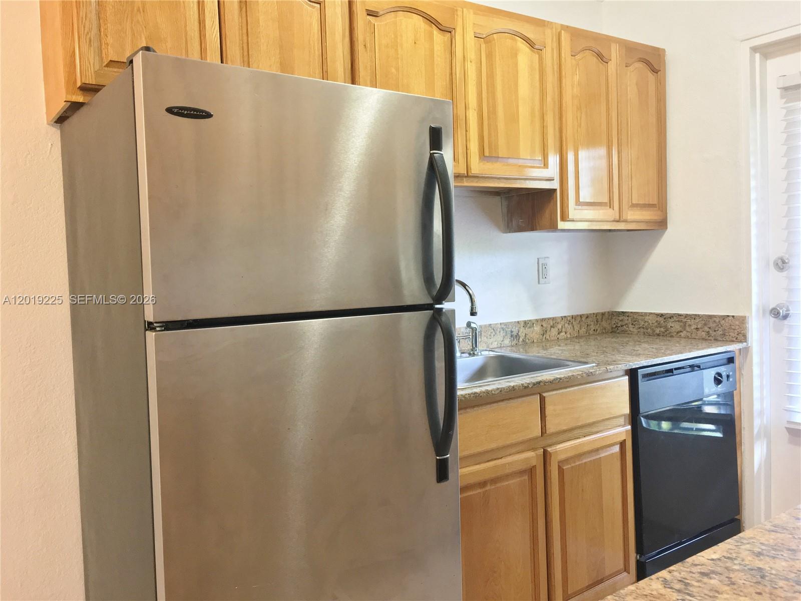 A kitchen features a stainless steel refrigerator, wooden cabinets, a sink, and a black dishwasher — 95 Edgewater Dr # 207, Coral Gables FL 33133, CORAL GABLES, FL