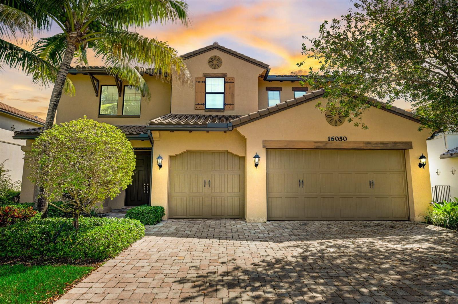 A two-story stucco house with a three-car garage and a paved driveway at sunset — 16050 Tuscany Estates Drive, Delray Beach FL 33446, DELRAY BEACH, FL
