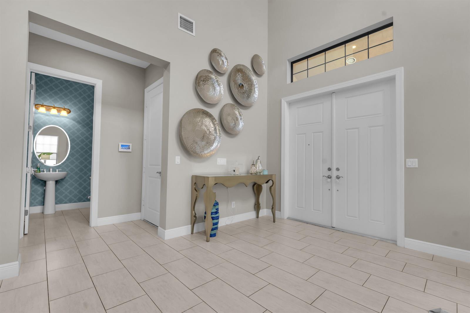 An entryway features a console table, wall-mounted metallic discs, and a doorway to a bathroom — 16050 Tuscany Estates Drive, Delray Beach FL 33446, DELRAY BEACH, FL
