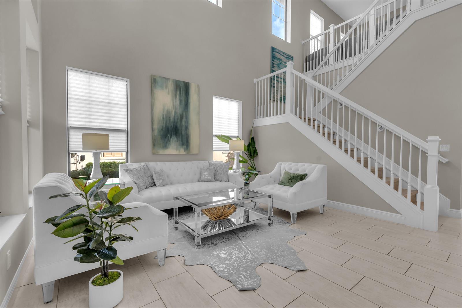 A bright living room features white tufted furniture, a glass coffee table, and a staircase — 16050 Tuscany Estates Drive, Delray Beach FL 33446, DELRAY BEACH, FL