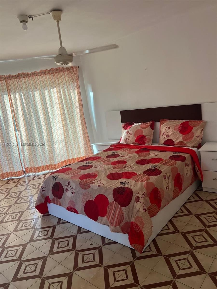 A bedroom features a bed with a patterned red comforter, tiled floors, and window curtains — No.10 Calle Bohechio, DR foreign, DR