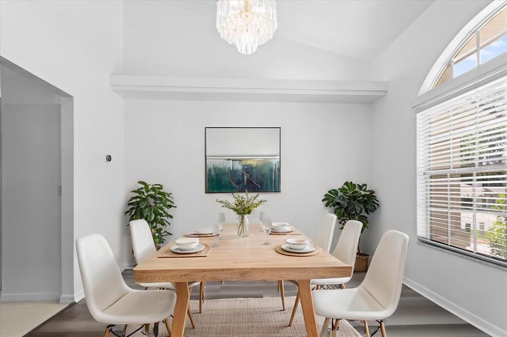 A dining room features a wooden table, six white chairs, a chandelier, and a large window — 10336 NW 13TH AVENUE, GAINESVILLE, FL