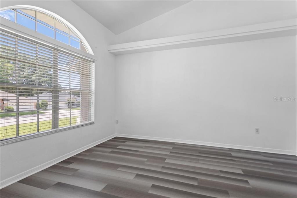 An empty room features gray wood-look flooring, white walls, and a large arched window — 10336 NW 13TH AVENUE, GAINESVILLE, FL