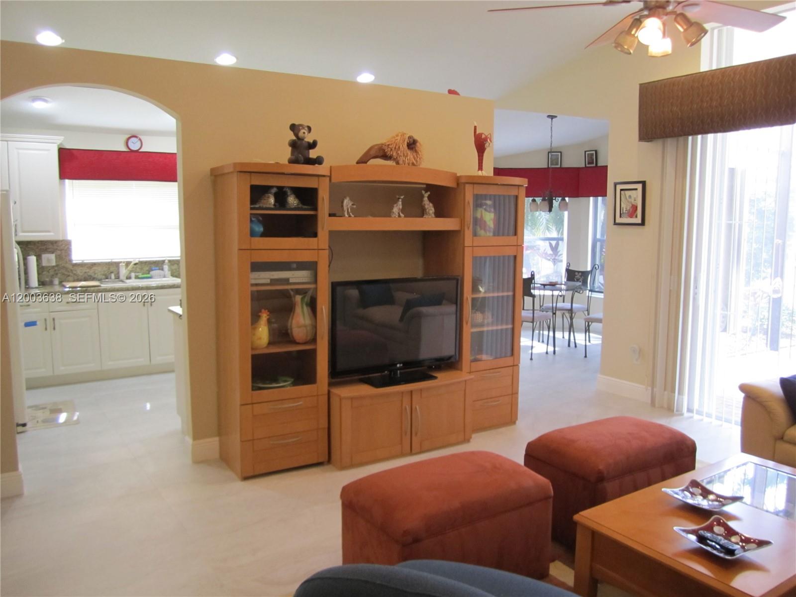 A living room features a wooden entertainment center, two red ottomans, and an adjacent kitchen — 9798 Casa Mar Dr, Lake Worth FL 33467, LAKE WORTH, FL