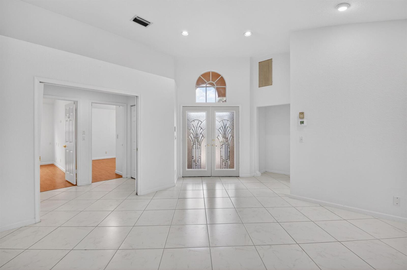 A bright entryway features white tile floors, double glass-paneled doors, and a high arched window — 7558 Ironbridge Circle, Delray Beach FL 33446, DELRAY BEACH, FL