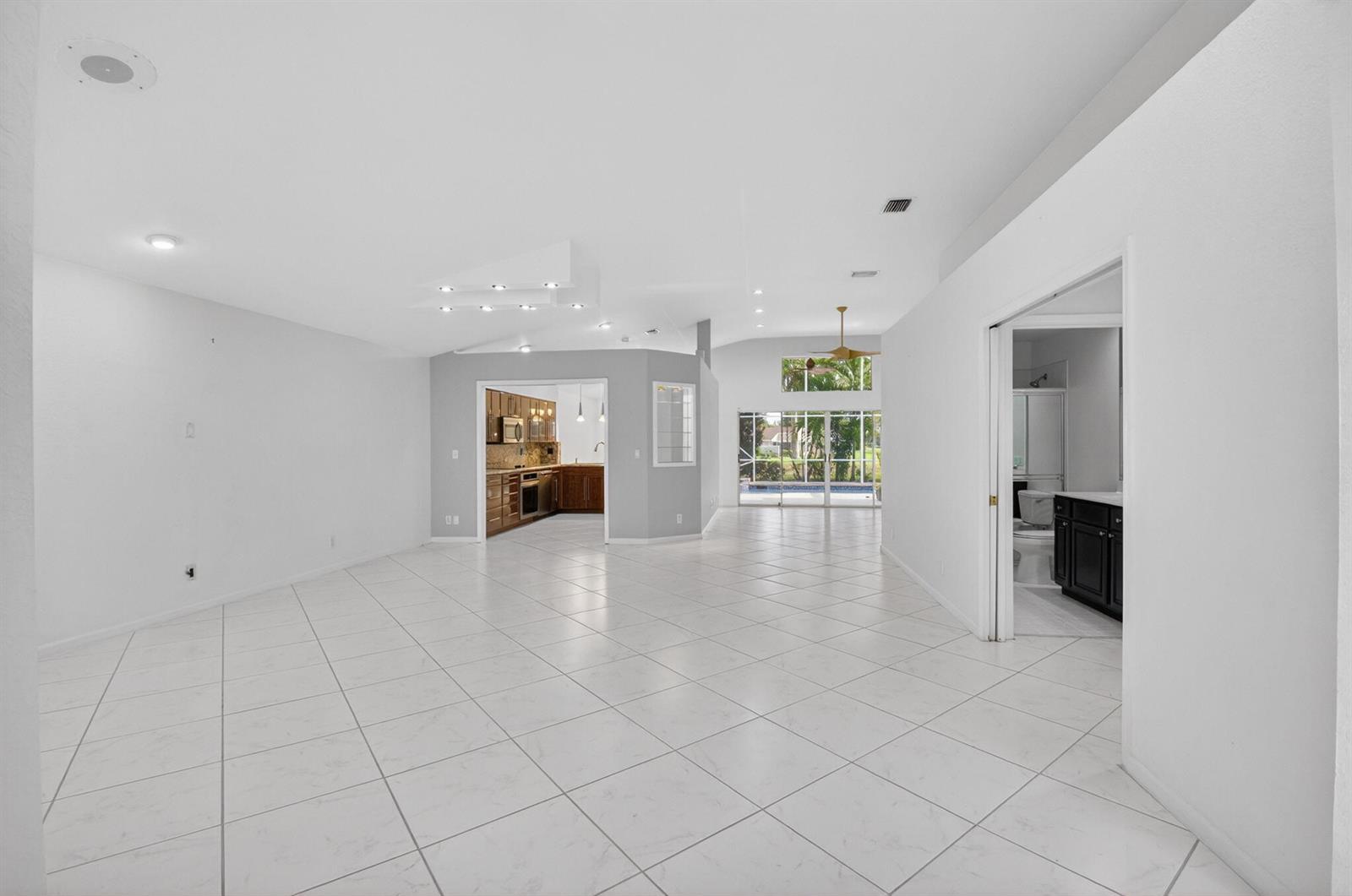 A spacious living area with white tile floors leads to a kitchen and sliding glass doors — 7558 Ironbridge Circle, Delray Beach FL 33446, DELRAY BEACH, FL